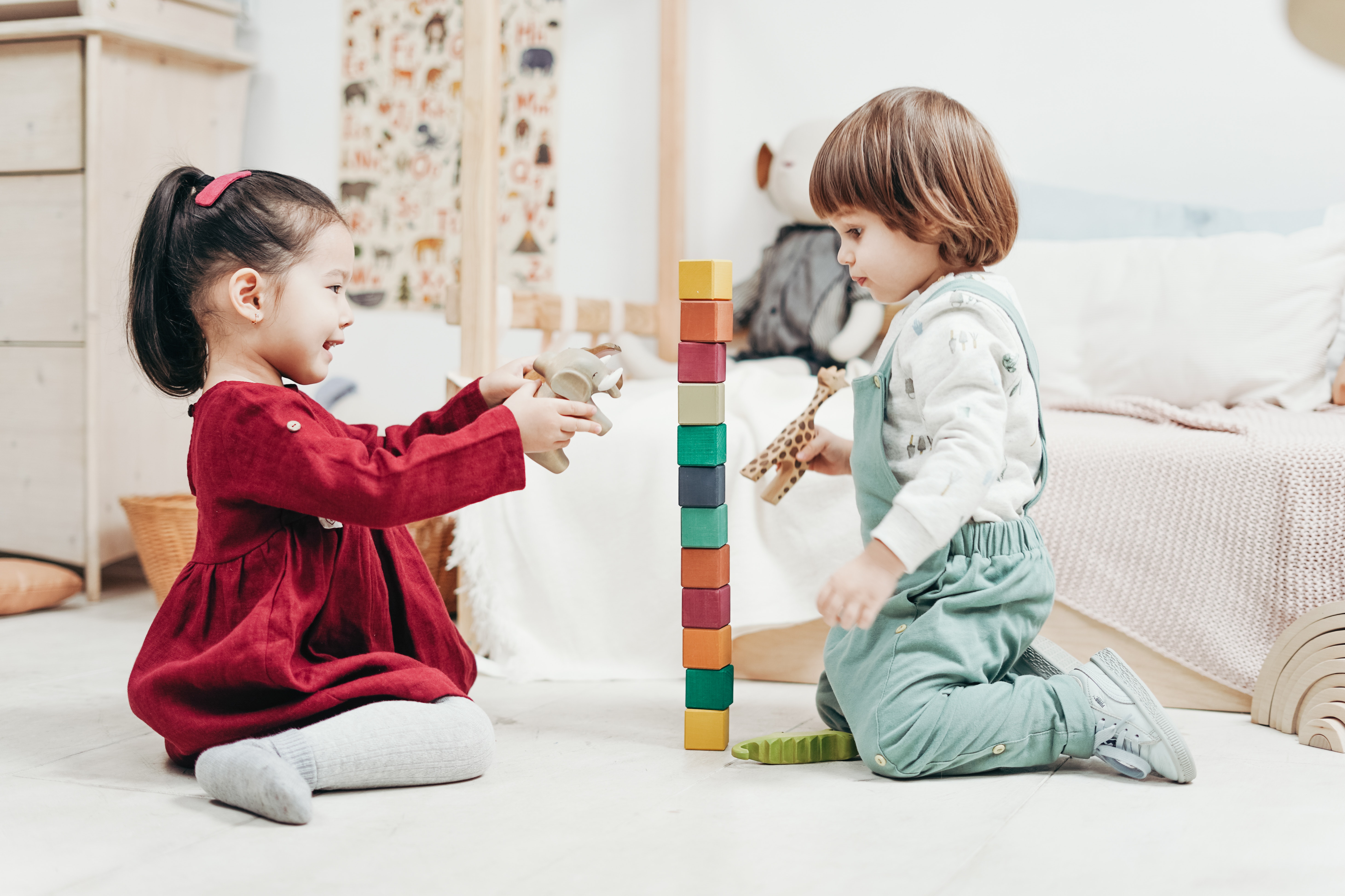 Two children facing each other. One is talking and they are playing with a tower of blocks.